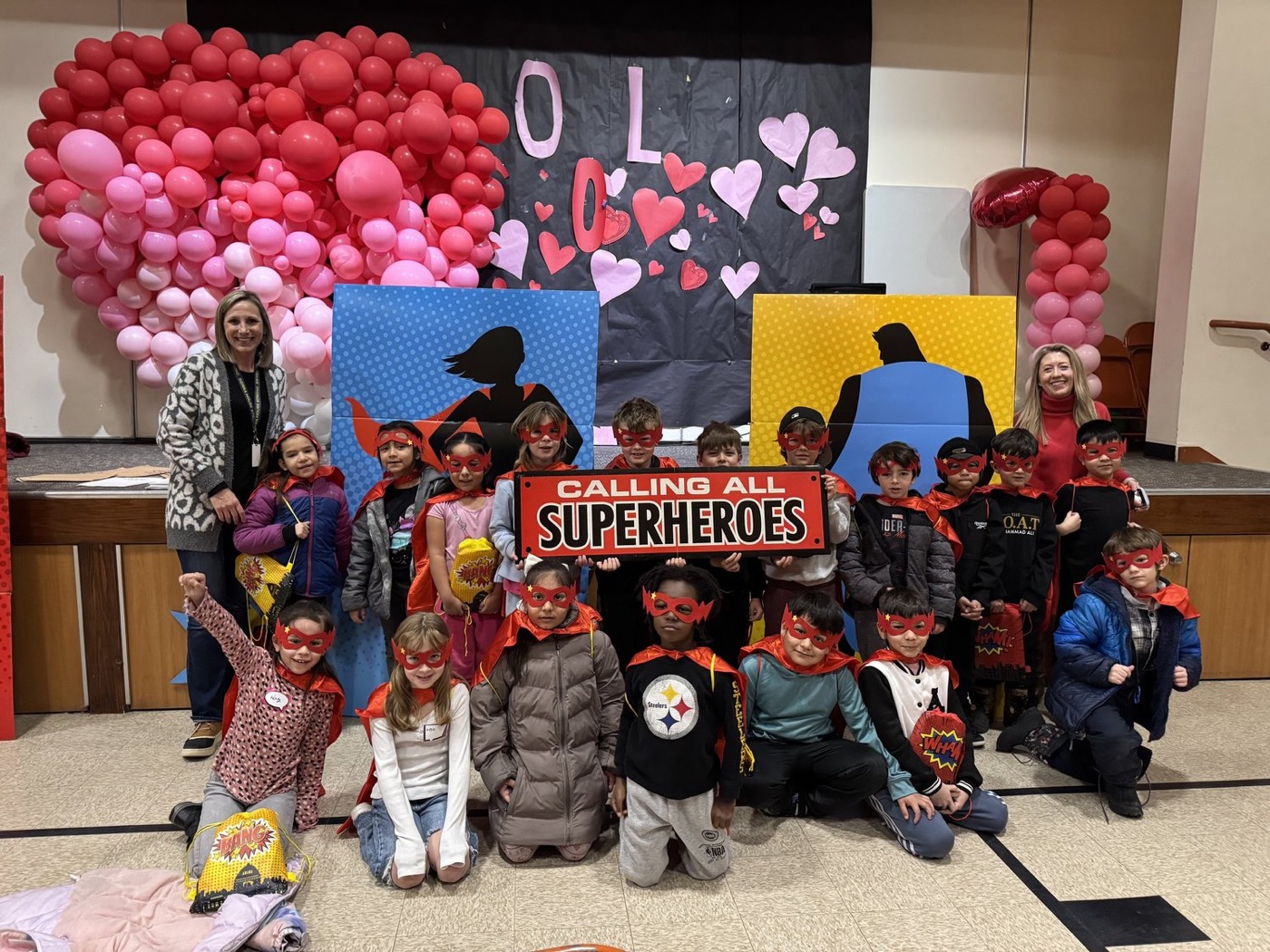 Second graders and volunteers posing in front of a Reading Superheroes banner